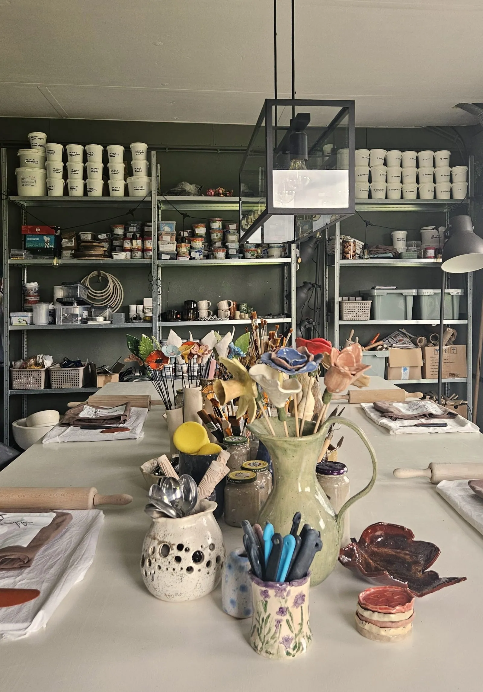 Werktafel met schappen vol glazuren, gereedschap en materialen in het atelier
